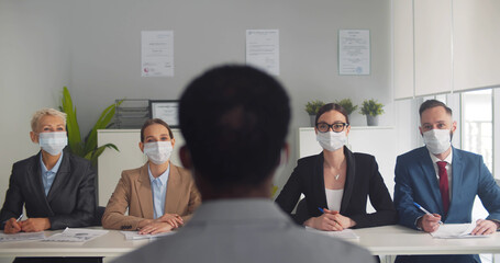Members of human resource team wearing protective mask while interviewing job candidate in office.