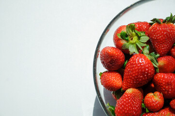 Red polish strawberries in a glass bowl on the white background with a copy space