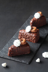 Contemporary Triangle Chocolate Vanilla Mousse Cakes, covered in chocolate with chopped almonds, decorated with whipped chocolate ganache and meringue cookies, on a dark gray background.
