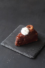 Contemporary Triangle Chocolate Vanilla Mousse Cakes, covered in chocolate with chopped almonds, decorated with whipped chocolate ganache and meringue cookies, on a dark gray background.