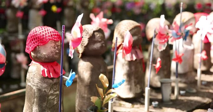 A slow motion of moving colorful windmills with Jizo statue daytime closeup