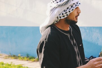 portrait of arab young man with ethnic male clothing , keffiyeh, the arabian head wrap and black thawb / tunic male clothing garment outdoors