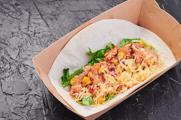 Tacos with meat, corn, cheese and lettuce in a craft container on an isolated dark background. Take away food. Photo for menu and site. Close up