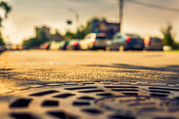 Summer in the city, the headlights of the approaching car on the avenue. Close up view of a hatch at the level of the asphalt