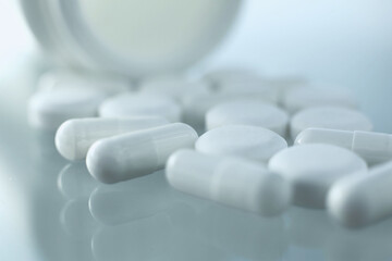 On a glass table lies a plastic bottle with medical pills scattered near