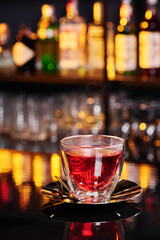 Beautiful transparent cup with red fruit tea on a shiny dark table on a blurred bar background. Close-up. Space