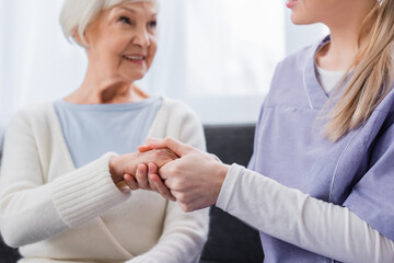 Obraz na płótnie Canvas nurse holding hand of aged woman smiling on blurred background