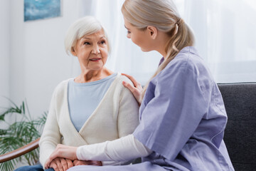 Obraz premium social worker touching hands of senior woman while talking at home