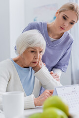 Fototapeta premium young social worker near aged woman looking at calendar on blurred foreground