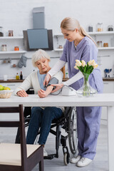 young nurse measuring blood pressure of handicapped woman in wheelchair at home