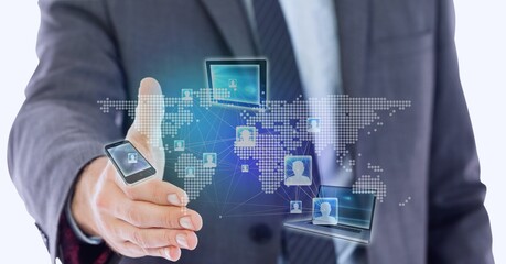 Electronic devices over world map against two businessman approaching to shaking hand