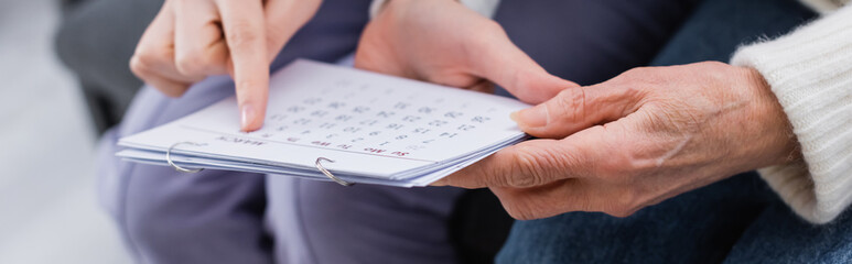 cropped view of social worker pointing at calendar near elderly woman suffering from memory loss, banner