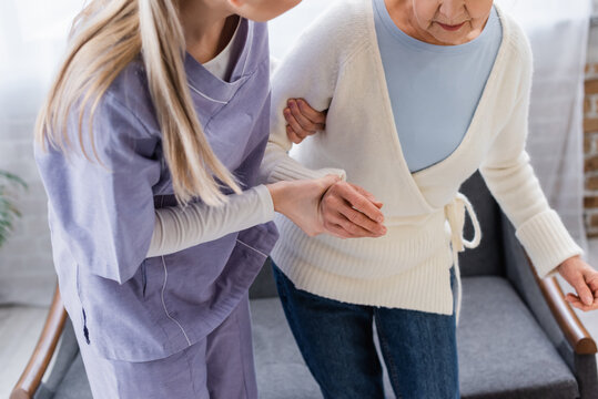 Partial View Of Social Worker Helping Elderly Woman Getting Up From Sofa At Home