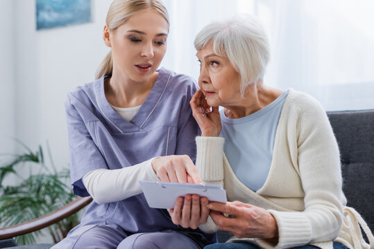 Young Nurse Pointing At Calendar Near Elderly Woman Sick On Dementia