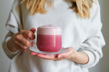 A cup of red velvet latte in the hands of a girl on a light background. Hot tasty drink. Trendy...