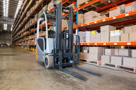 View of big warehouse, forklift standing near high shelves filled woth packages