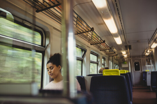 Mixed race woman in white sweater sleeping by window sitting on train