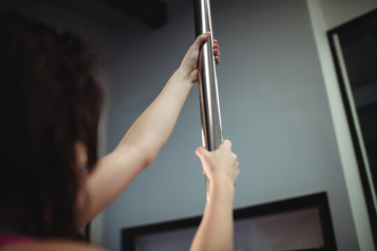 Caucasian woman exercising, holding on to metal pole at pole dance and fitness studio