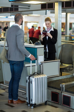 Caucasian airport worker checking documents of man with suitcase