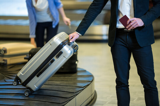 Midsection of caucasian man picking up suitcase from luggage return tape