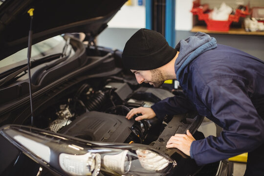 Caucasian male car mechanic looking under car mask, at engine