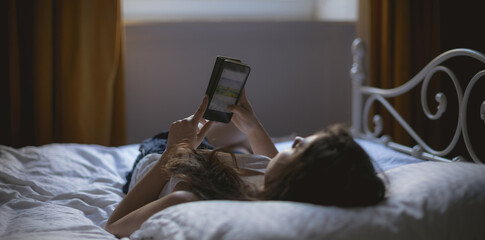 Caucasian woman lying on bed and using smartphone at home