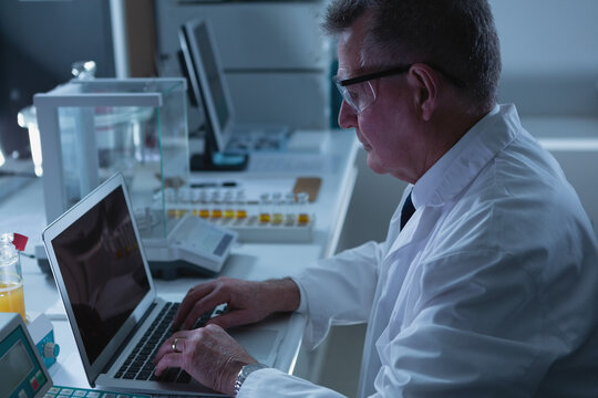 Caucasian male scientist in protective glasses working in laboratory using laptop