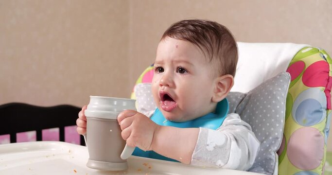 Cute baby boy drinking a glass of water at home. Close-up. The child drinks water from a plastic sippy cup