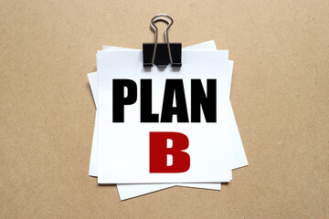 Plan B, text on the sticker. the paper is clamped with a clerical clip. paper on wood background.