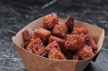 dark croutons in a craft container on an isolated dark background. Take away food. Photo for menu and site. Close up. High quality photo