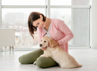 Beautiful woman petting lovely little dog in light room