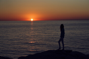 Fototapeta premium sunset in the mountains by the sea and a female silhouette on the beach