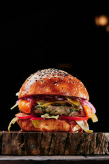 Beef burger with cheese, tomatoes, red onions, cucumber and lettuce on wooden cut on black...