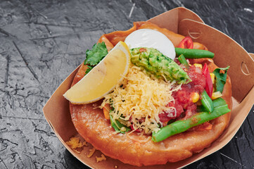 Fried tortilla with Mexican filling with asparagus, poached egg, guacamole and cheese in a craft container on an isolated dark background. Take away food. Photo for menu and site.