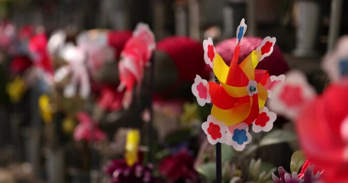 A slow motion of moving colorful windmills with Jizo statue daytime closeup