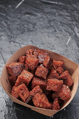 dark croutons in a craft container on an isolated dark background. Take away food. Photo for menu and site. Close up. High quality photo