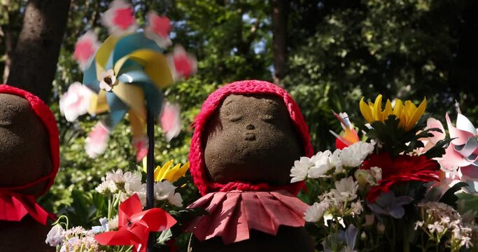 A slow motion of moving colorful windmills with Jizo statue daytime closeup