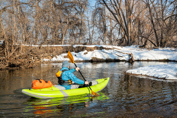 senior male paddler is paddling an inflatable whitewater kayak on a small river - Poudre River in Fort Collins, Colorado, winter or early spring scenery