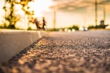 Sunset in the city, the pedestrians walking on the sidewalk. Close up view of a level curb on the road - obrazy, fototapety, plakaty