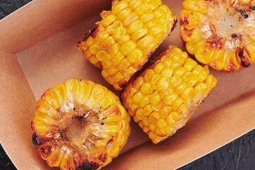 grilled corn in a craft container on an isolated dark background. Photo for menu and site. space for text. Close up
