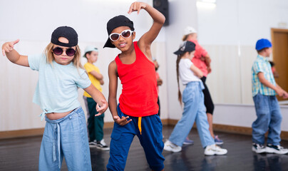 Tween blonde girl and boy in caps and sunglasses dancing hip-hop in group lesson in dance school..