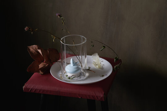 Vase with decor and faded flowers on round shaped plate with feather on gray background