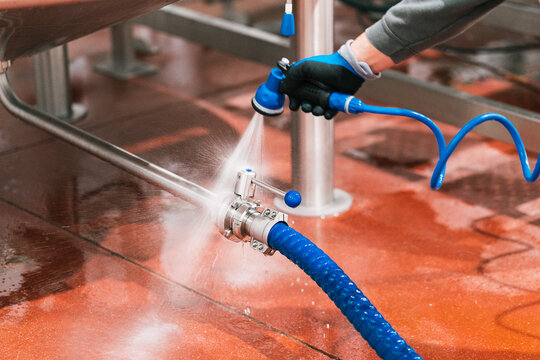 Crop unrecognizable male worker in mask washing valve of metal tank at work in brewing company
