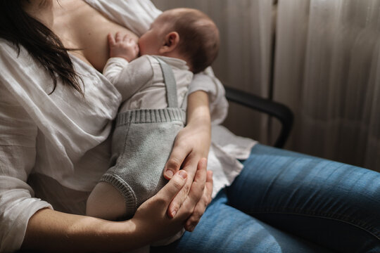 Cropped unrecognizable adult mom in casual wear suckling charming little child while sitting in light house room
