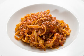 Italian tagliatelle topped with meat and tomato sauce, close-up in a white plate