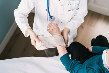 High angle of crop anonymous doctor in uniform wrapping gauze around wrist of patient in hospital