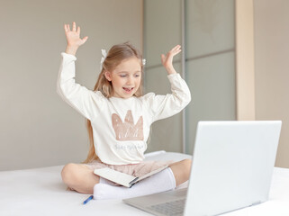Happy little girl learning online with laptop at home. 5 years old girl doing online school classes. Online education concept.