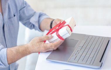 Man holding gift by computer. Online dating or online celebration concept.
