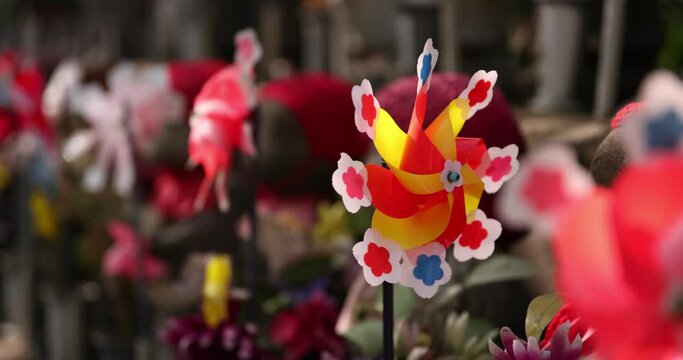 A slow motion of moving colorful windmills with Jizo statue daytime closeup