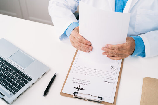 Top view of crop unrecognizable male doctor working at table with paper form and netbook against stethoscope in hospital